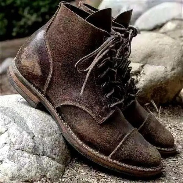 Dark brown lace-up ankle boot resting on rocks, showing its side profile, stitched panels, and textured cap toe.