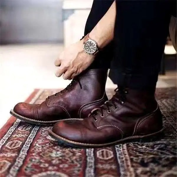Pair of deep brown lace-up ankle boots worn indoors on a patterned rug, with visible ankle height and contrasting toe stitching.