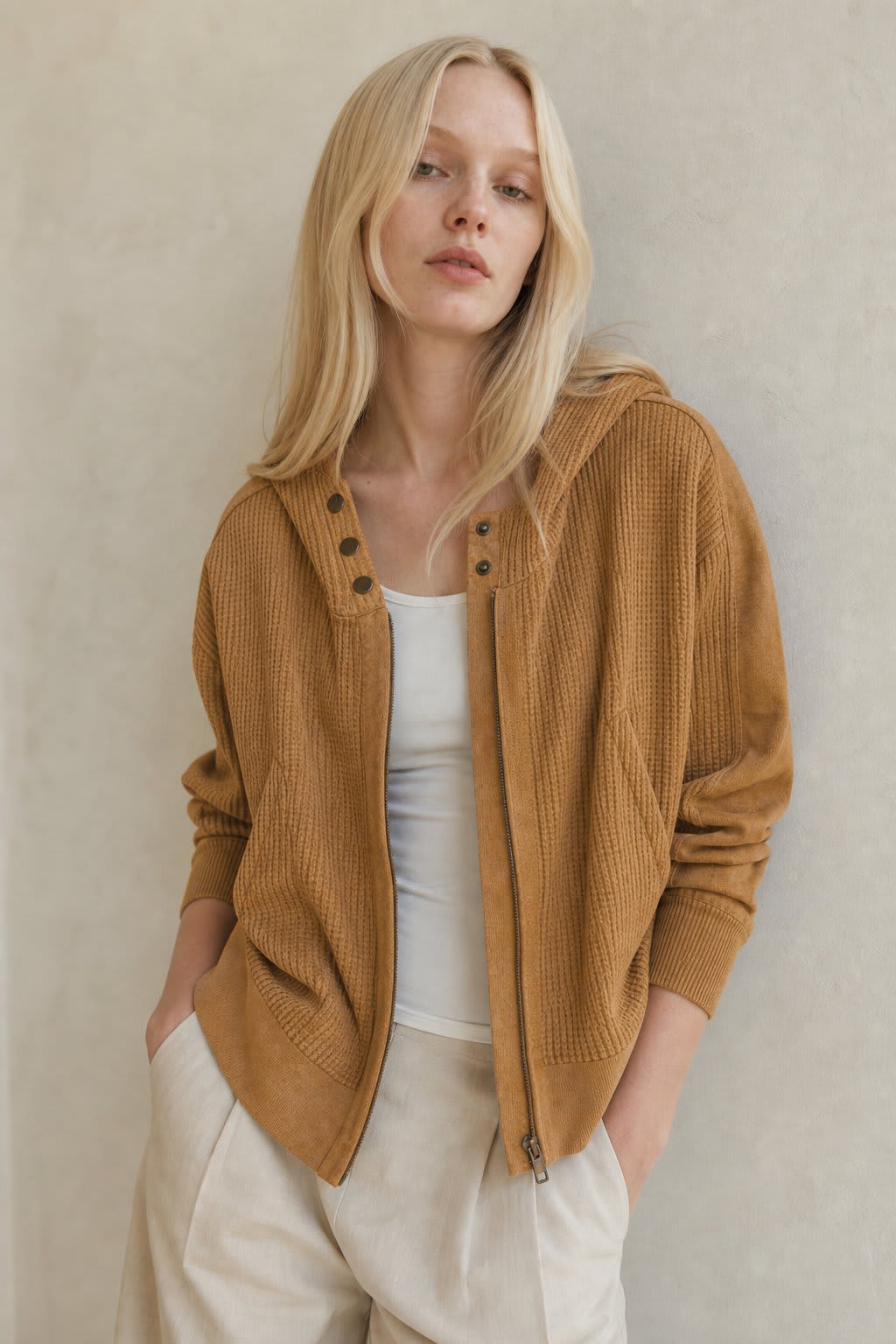 Model wearing an olive green waffle knit zip-up hoodie with cropped length and hood, styled with brown pants._10