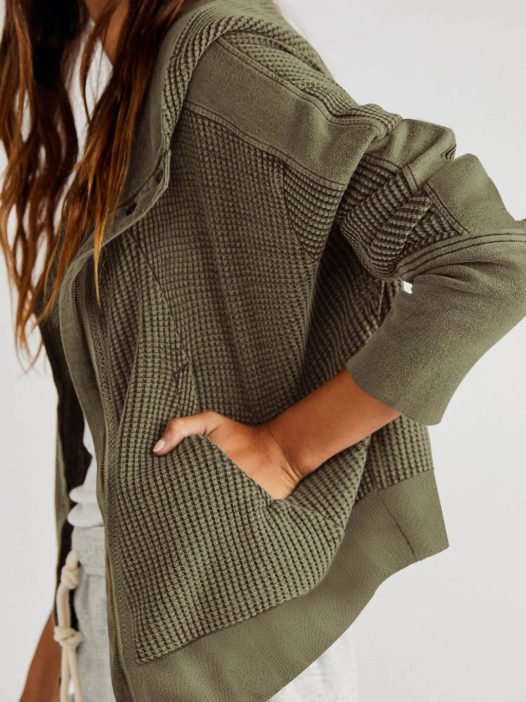 Model wearing an olive green waffle knit zip-up hoodie with cropped length and hood, styled with brown pants._18