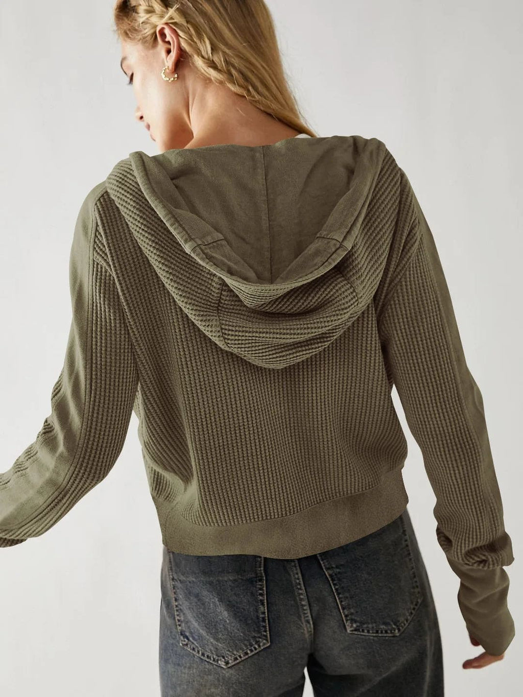 Model wearing an olive green waffle knit zip-up hoodie with cropped length and hood, styled with brown pants._19