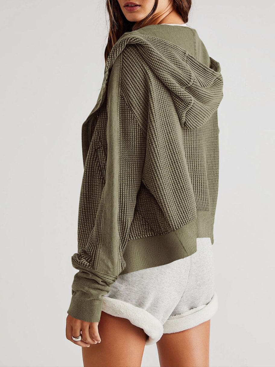 Model wearing an olive green waffle knit zip-up hoodie with cropped length and hood, styled with brown pants._21