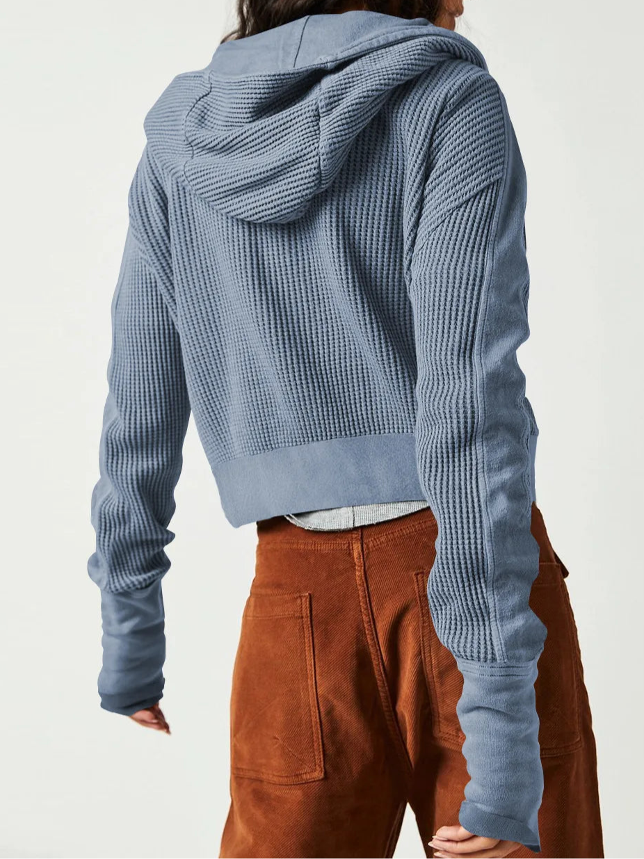 Model wearing an olive green waffle knit zip-up hoodie with cropped length and hood, styled with brown pants._25