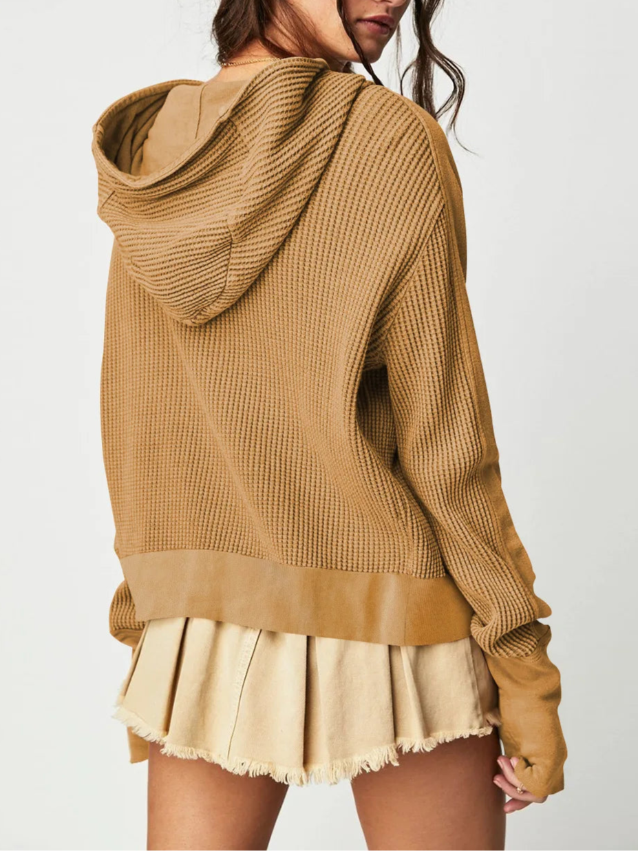 Model wearing an olive green waffle knit zip-up hoodie with cropped length and hood, styled with brown pants._55
