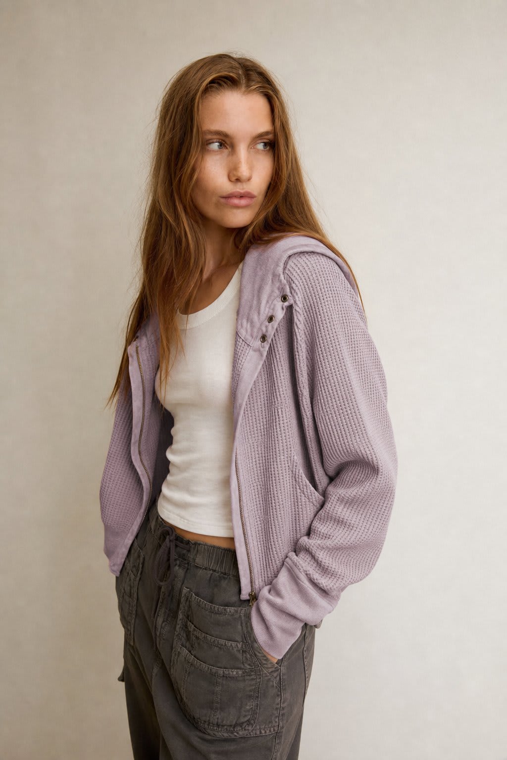 Model wearing an olive green waffle knit zip-up hoodie with cropped length and hood, styled with brown pants._6