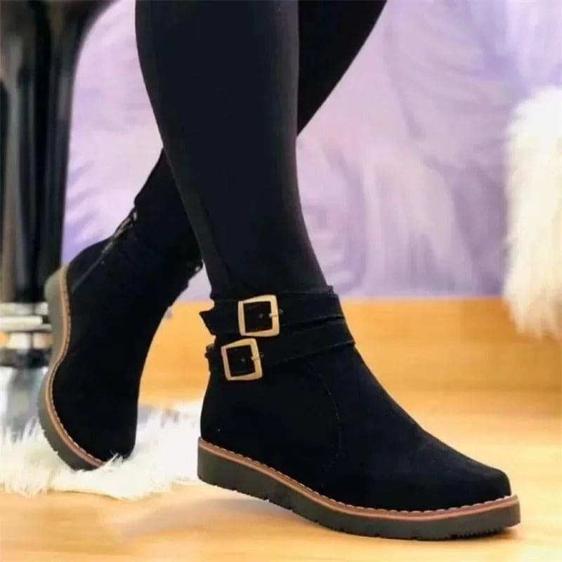 Woman wearing ankle boots with double buckle detail and flat sole, styled with dark leggings on a wooden floor._0